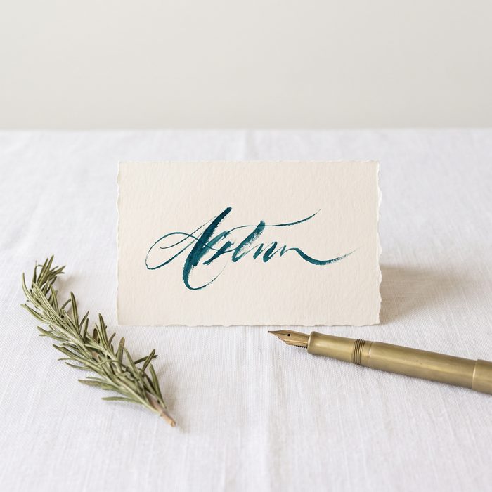 A handwritten place card in teal ink on linen
